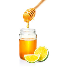 honey in glass jar with wooden honey dipper and cut lime on white background