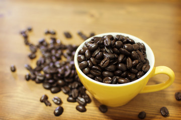 Roasted coffee beans in yellow cup on wooden table.