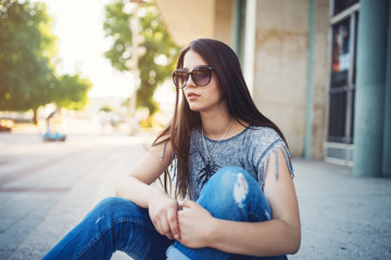 Urban vintage portrait of beautiful and attractive girl with sunglasses and headphones. She walks and listens to music. Warm summer colors and haze. Strong back light.