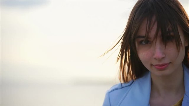 Portrait of an adult and beautiful girl who is near a river or a lake, the hair of this tranquil female waving under the gusts of the wind