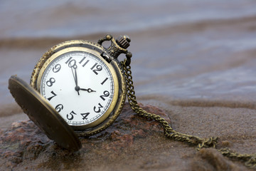 round pocket watch with hands and a chain on the stone against water