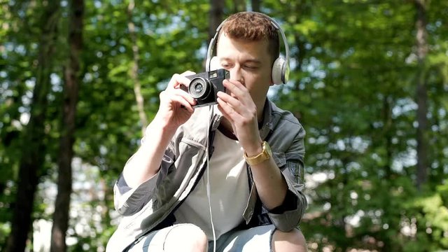 Young man listening music and doing photos on old camera in the park, steadycam shot
