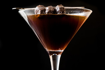 Black Manhattan Cocktail with olives on dark wooden surface.