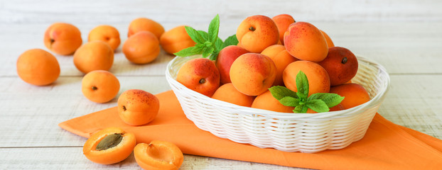 Ripe apricots in a basket on a light wooden background.