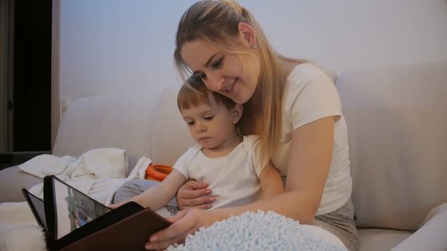 Mother with baby son looking family photo album before going to sleep