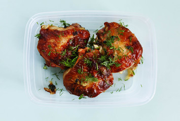 Fried chicken thighs with greens in a storage container on a blue background. Ruddy crust.