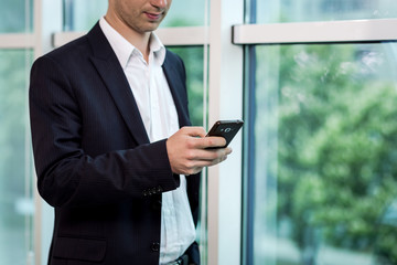 Fototapeta premium Businessman holding a cell phone and writing sms message in office,businessman use mobile smart phone,Close up of a man using mobile phone,Young businessman working with modern devices mobile phone.