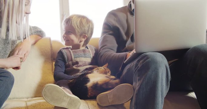 modern family little girl playing with cat and mom while dad works with notebook on couch indoor in modern industrial house. caucasian. 4k handheld slow motion video shot