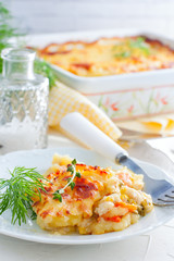 Portion of potato casserole with vegetables on a white plate, selective focus