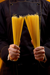 Immagine verticale dettaglio mani di un cuoco in divisa che tiene in mano degli spaghetti crudi