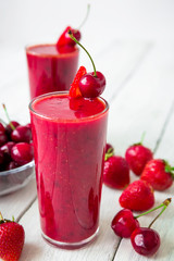 Cherry and strawberry smoothie and tasty berries on white rustic table. Tasty milkshake