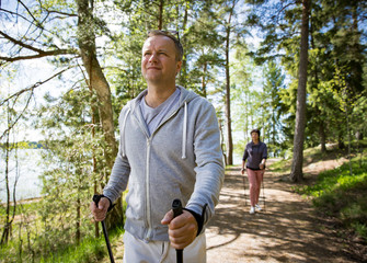 Summer sport in Finland - nordic walking. Man and mature woman hiking in green sunny forest. Active...
