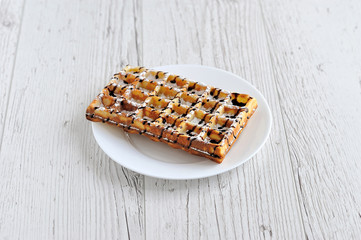 Wafers with powdered sugar covered with chocolate on a white plate on a wooden table