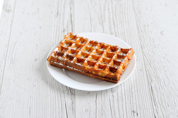 Wafers with powdered sugar covered with caramel on a white plate on a wooden table