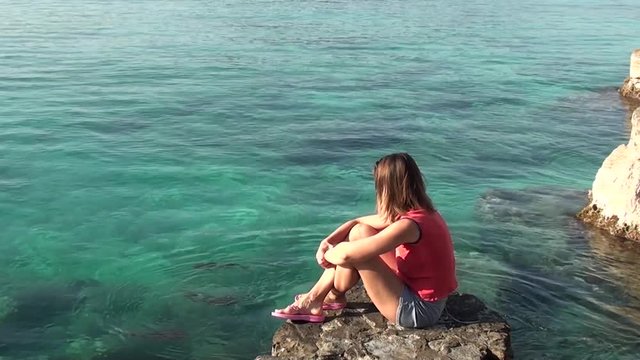 Young Woman sits on a rock and watches squids in the water