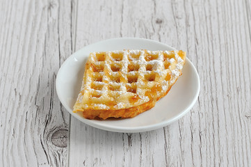 Wafers with powdered sugar covered with honey on a white plate on a wooden table