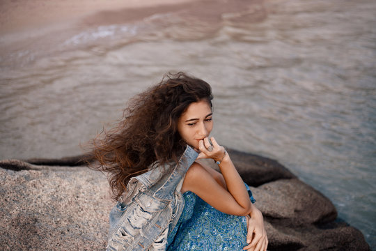 stylish young romantic woman sitting on stone at the beach