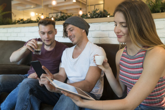 Three friends using tablet and cell phone in a cafe