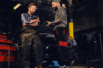 Two bearded  mechanics inspecting car's engine parts.