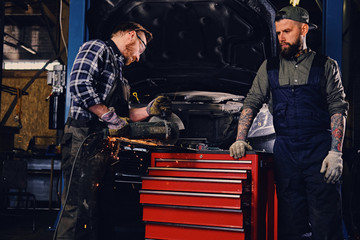 Fototapeta na wymiar Two b mechanics working with an angle grinder in a garage.
