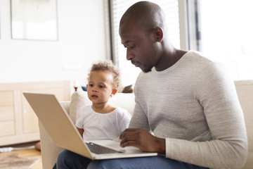 Afro-american father with little daughter at home holding laptop.