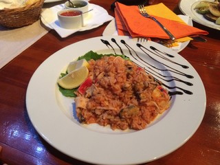 Decorated plate of rice with seafood, lemons and salad leaf on wooden table with sauce, plates, forks background