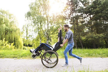 Hipster son running with disabled father in wheelchair at park.