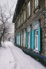 Bright vividly blue window. Wooden blue window in a wooden house in the winter. Snow on the ground and tree without leaf. No body on the snow footpath, only bright blue windows. 