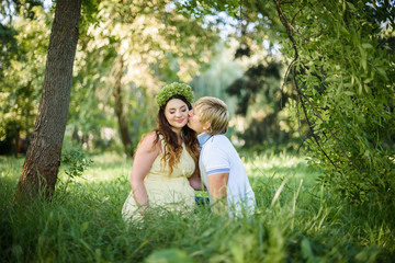pregnant woman with husband kissing on green grass in the park