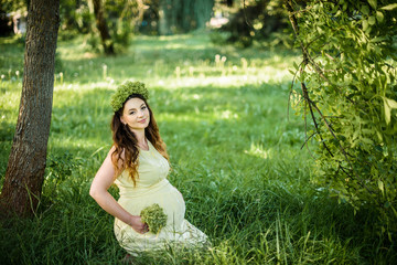 Naklejka na ściany i meble Pregnant woman in the park in the summer park. A girl prepares to become a mother. Pregnant woman in the fresh air.
