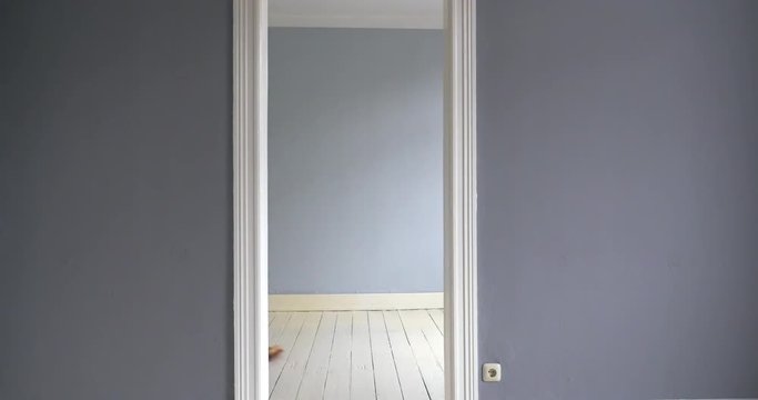 A man sweeps the floor of an empty room. Filmed through an open door in the center of the image.