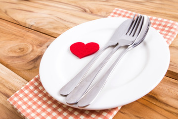 red heart shape with White empty plate with fork and spoon on wooden table for love dinner concept