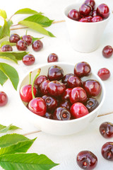 Berries of fresh cherry with cherry green leaves on an old white wooden background