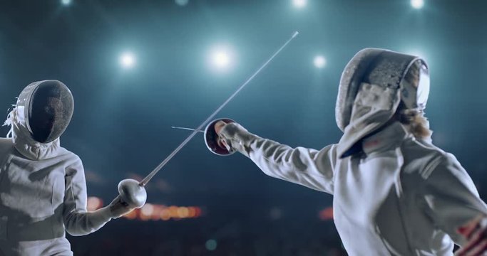 4K video in slow motion of two female fencing athletes. The action takes place on professional sports arena with spectators and lense-flares. Women wear unbranded sports clothes. Arena is made in 3D.