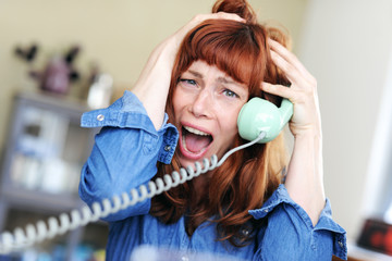 Frau mit roten Haaren und Pony  telefoniert mit einem alten Telefon und ist dabei emotional und rauft sich die Haare