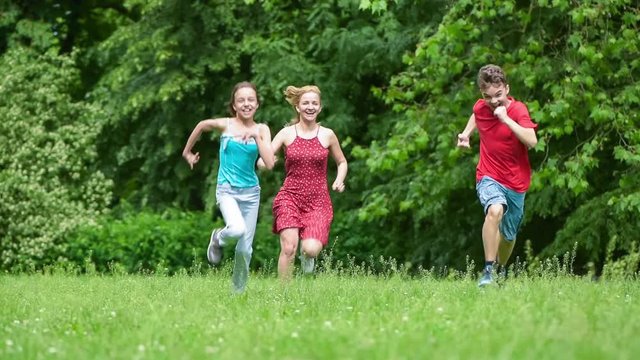 Happy family - mother, boy and girl running through the field towards the camera. People run and smiling by in grass at summer park.