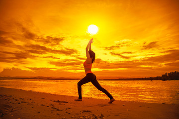 Silhouette healthy woman doing Yoga exercises on the beach in sunset time, Thailand.