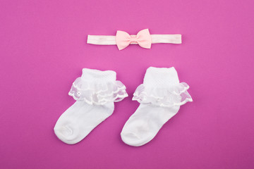 Set for girl baby. On a purple background. Top view. Flat lay, Delicate baby girl headband, socks, close-up. Newborn gifts.