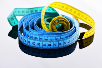 Rolls of colorful tape measures on grey surface with reflection