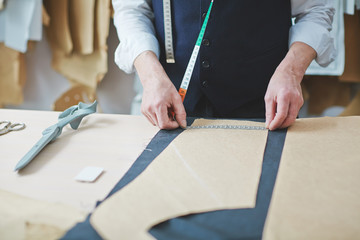 Portrait of unrecognizable skilled tailor working in atelier: measuring patterns on fabric while...