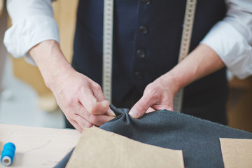 Portrait of unrecognizable skilled tailor working in atelier: pinning and stitching fabric while...