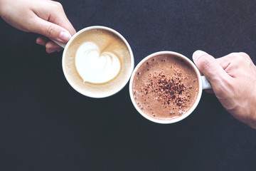 Top view image of man and woman's hands holding coffee and hot chocolate cups with wooden table...