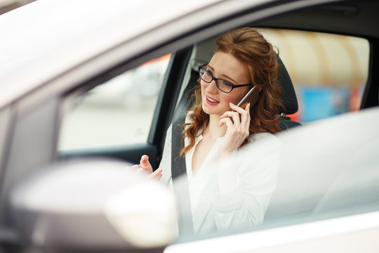 Attractive red hair businesswoman talking on the phone while waiting in the car.