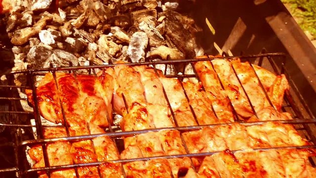 Add chicken legs on a grill. The camera slides along the grill with chicken and meat. Smoke rises from the coal through the meat