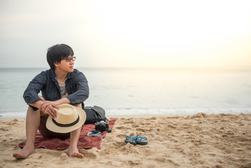 Young Asian man sitting on tropical beach and see the beautiful sunset, happy vacation time and summer holiday travel concepts