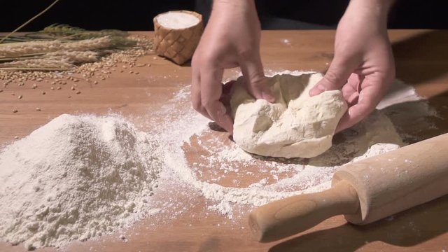The cook kneads the dough with both hands on the flour-poured table