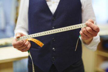 Closeup shot of unrecognizable tailor holding measuring tape in hands while working in traditional...