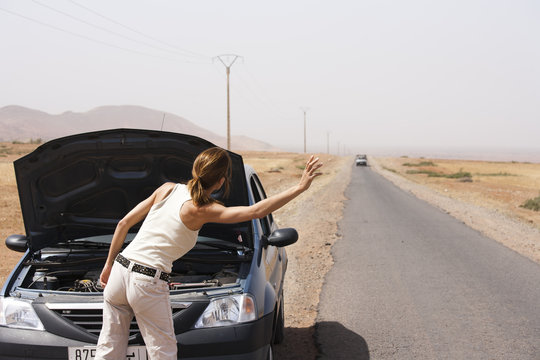 femme en panne de voiture qui fait des signes au milieu du désert 