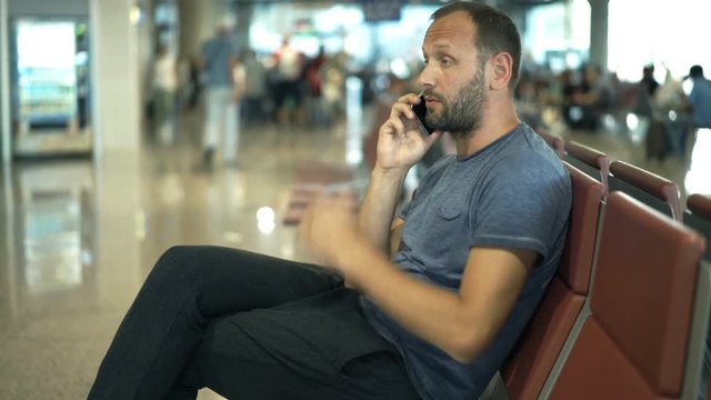 Angry man talking on cellphone and waiting for late plane at airport 
