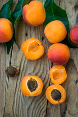Fresh ripe colorful apricots halved and whole on weathered plank wood background, kernel, green leaves, top view